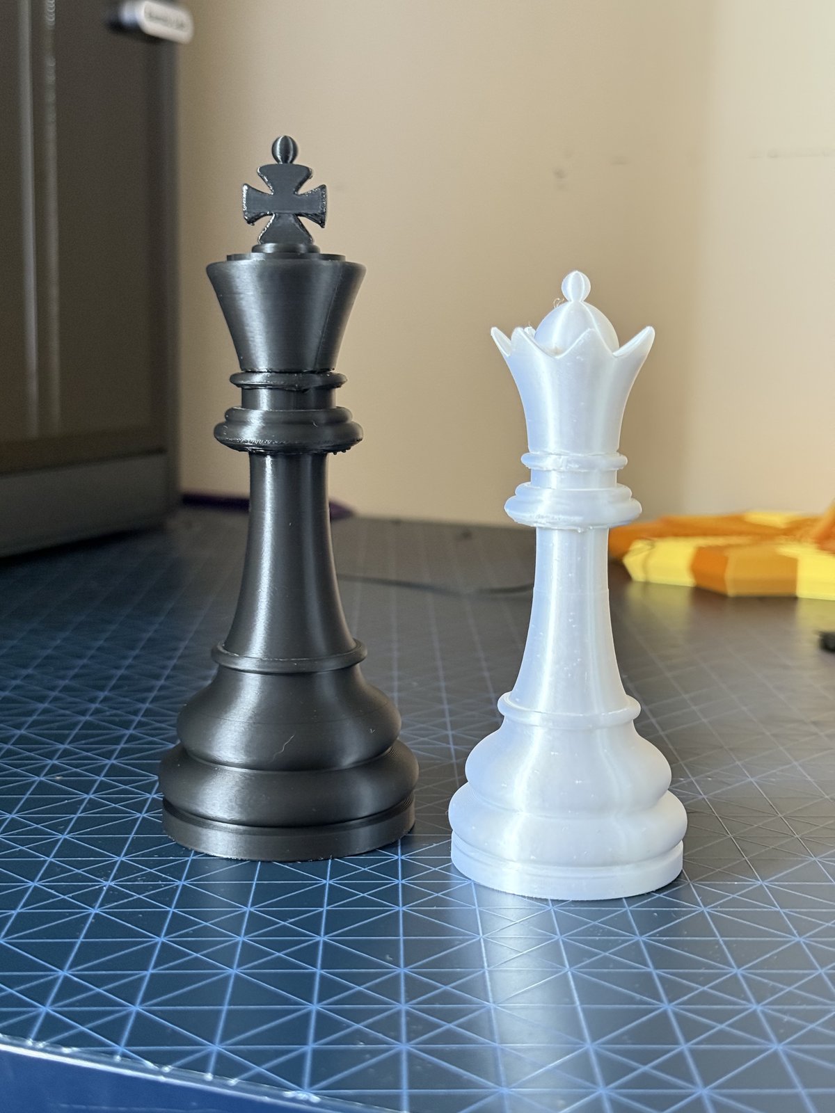 A large black 3D-printed chess king and white chess queen standing side by side on a cutting mat