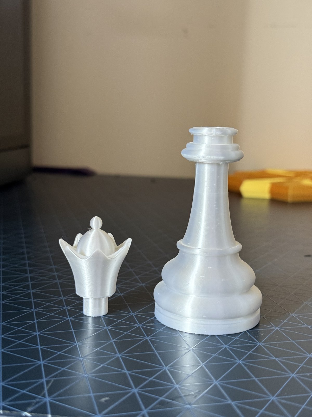 The white chess queen split into its two printed parts, the crown top and the body, laid side by side before assembly