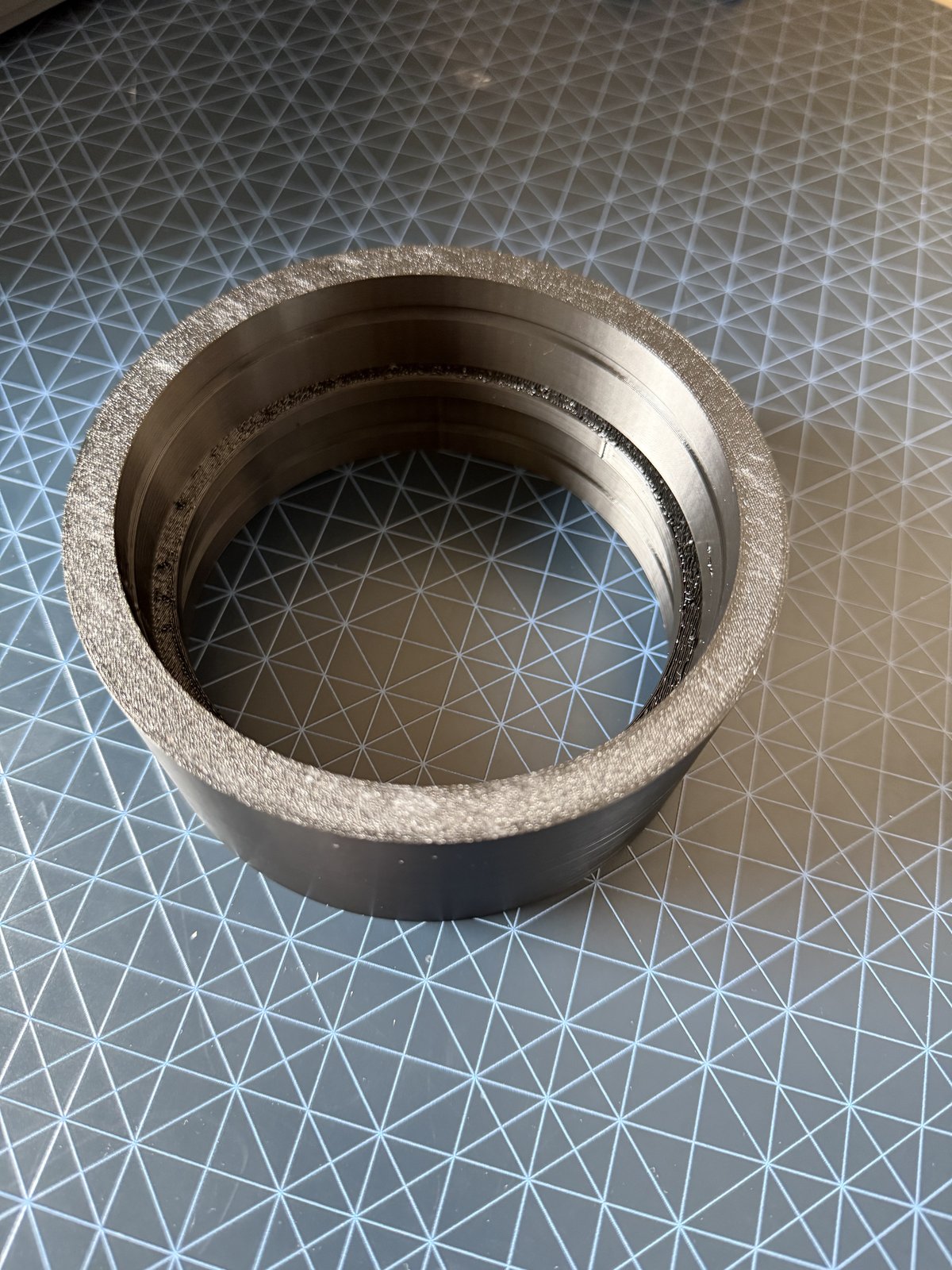 A cylindrical 3D-printed bushing with a textured outer surface and smooth inner bore, sitting on the printer's build plate
