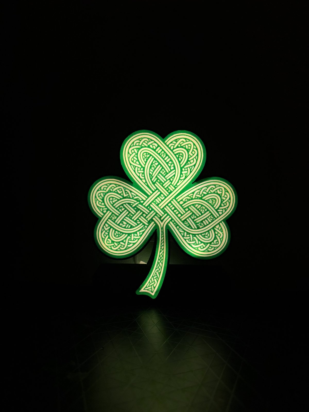A Celtic knotwork shamrock with a backlit LED, glowing green against a dark background