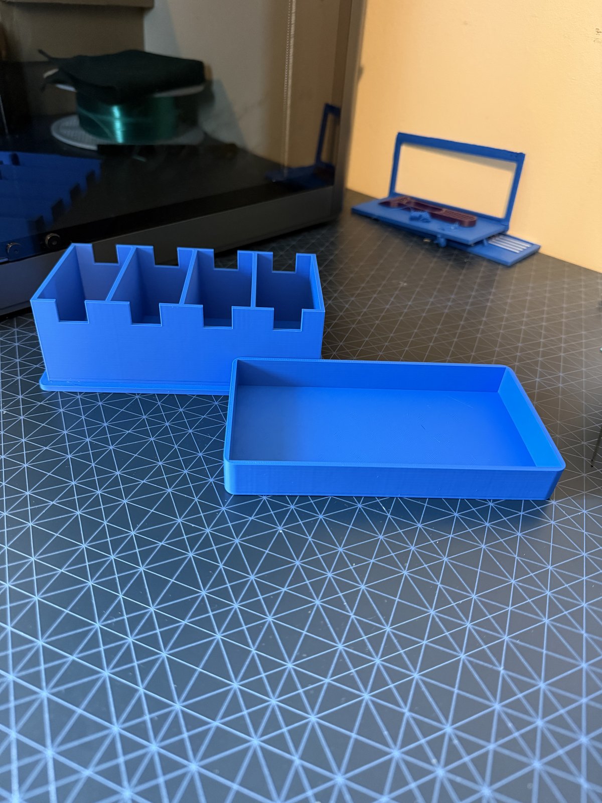 A blue 3D-printed two-part storage box, one flat tray and one stepped compartment section, sitting side by side