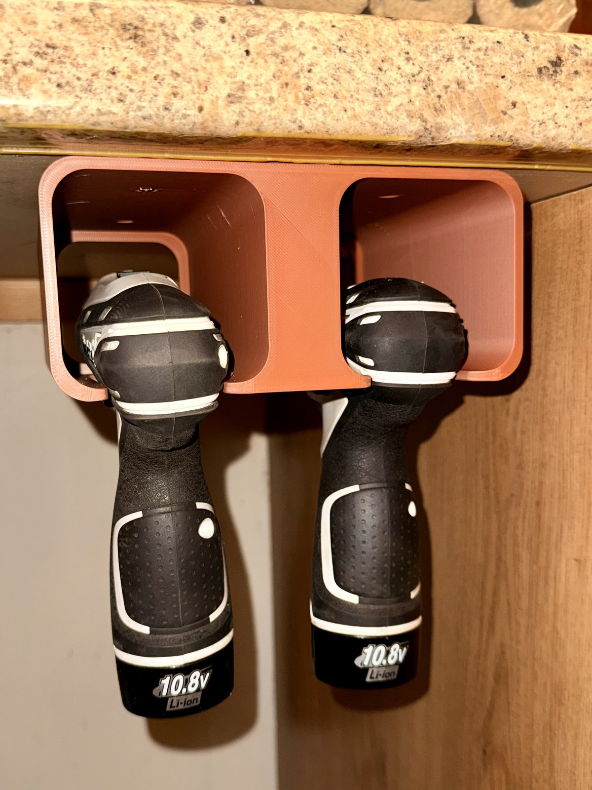 A terracotta 3D-printed under-counter caddy holding two cordless drills by their handles